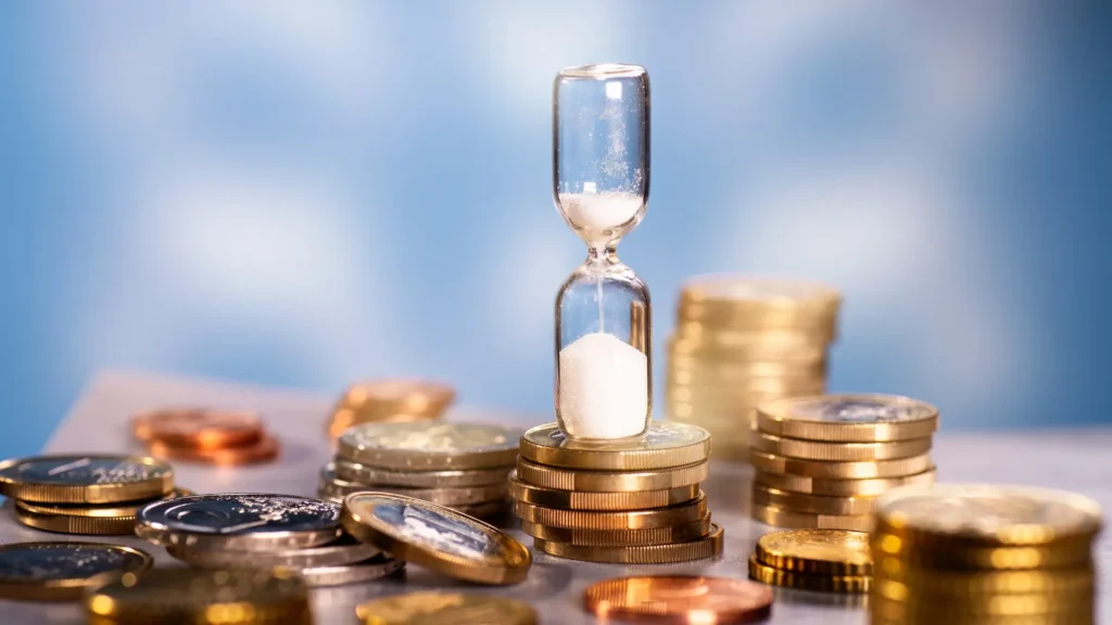 Un sablier dont le sable s'écoule, posé sur une pile de pièces de monnaie en euro, symbolisant l'impact de l'inflation et la perte de valeur de l'argent dans le temps.